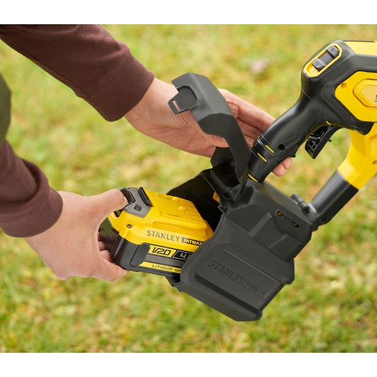STANLEY SFMCPC93M1 battery being inserted into yellow and black power tool outdoors.