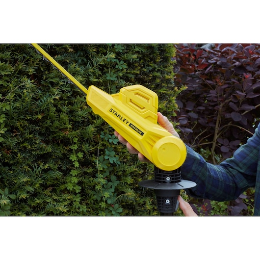 Photo of STANLEY SFMCPH845B hedge trimmer in use, yellow body, person trimming green hedge outdoors.