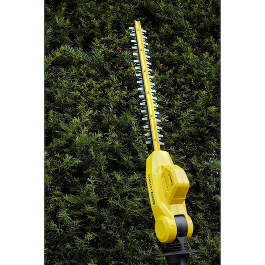Stanley SFMCPH845B yellow cordless pole hedge trimmer cutting greenery, outdoor angle.