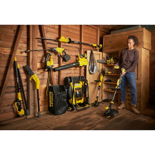 STANLEY SFMCPH845M1 corded and cordless garden tools set in shed, person holding string trimmer.