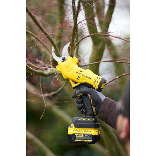 STANLEY SFMCPP32B cordless pruner cutting tree branches, yellow and black, outdoor use.
