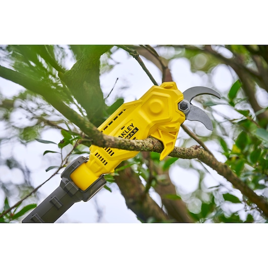 STANLEY SFMCPP632D1 yellow cordless pruning shears cutting a tree branch outdoors.