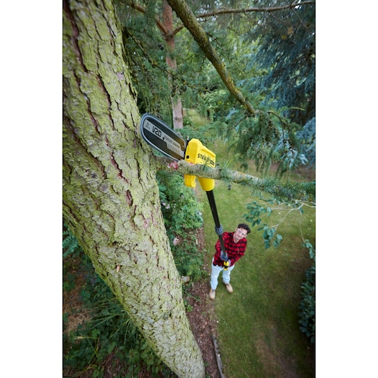 STANLEY SFMCPS620B pole saw cutting high tree branch outdoors, yellow and black tool in use.