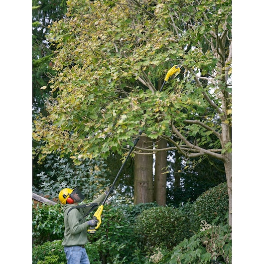 STANLEY SFMCPS720M1 pole saw used outdoors to trim tall tree branches, person wearing safety gear.
