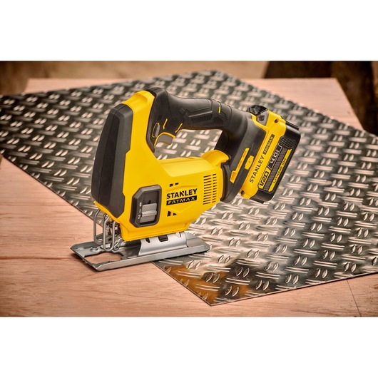 Photo of STANLEY SFMCS600B jigsaw on a metal sheet, yellow and black cordless power tool, side view.