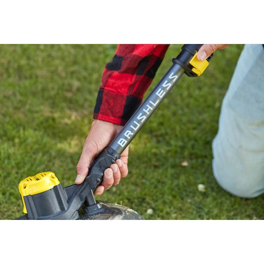 STANLEY SFMCSTB933B brushless string trimmer close-up, showing handle and yellow battery in outdoor use.