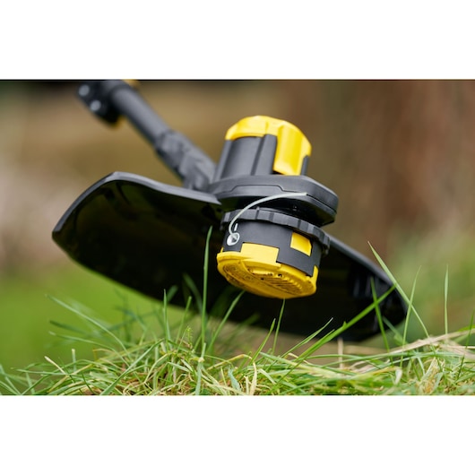 STANLEY SFMCSTB933M string trimmer head close-up outdoors, black and yellow design, grass visible.