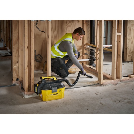 Stanley V20 vacuum being used by a worker to clean construction site debris inside a wooden framed room.