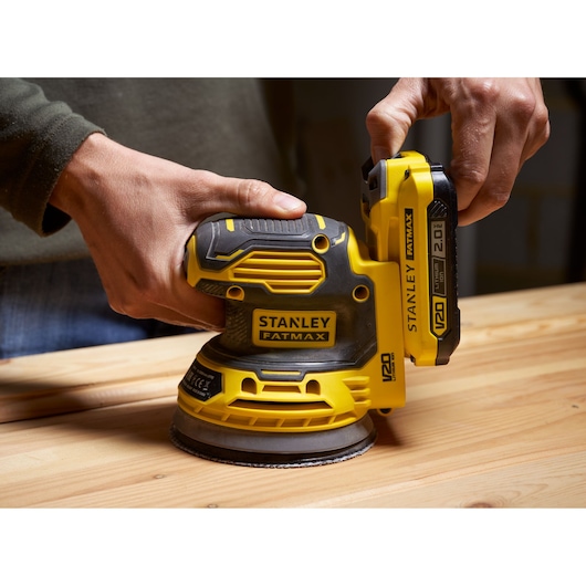 Photo of STANLEY SFMCW220B cordless orbital sander in use on wooden surface.