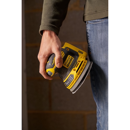 STANLEY SFMCW220B palm sander held in hand, yellow and black, close-up side angle.