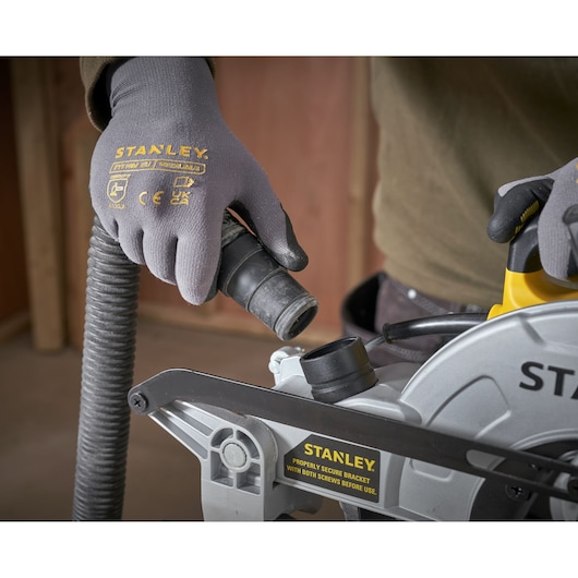 STANLEY SM1650 miter saw close-up with gloved hands connecting dust extraction hose.