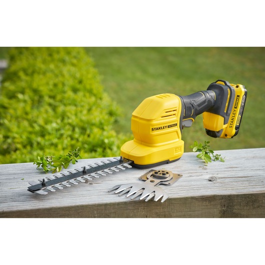 STANLEY STCSS20D1 cordless shrub shear and grass trimmer in yellow shown outdoors with attachments.