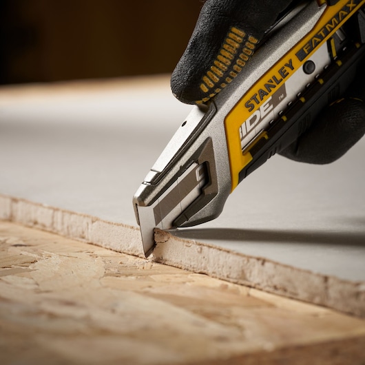 Photo of STANLEY STHT0-11818 utility knife cutting drywall, close-up detail, yellow and silver handle.