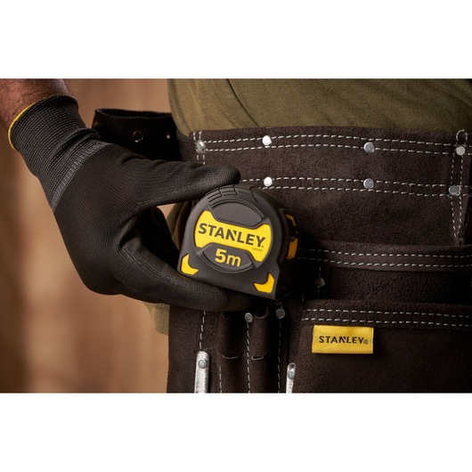 STANLEY STHT0-33561 tape measure, black and yellow, in tool belt, photography close-up.