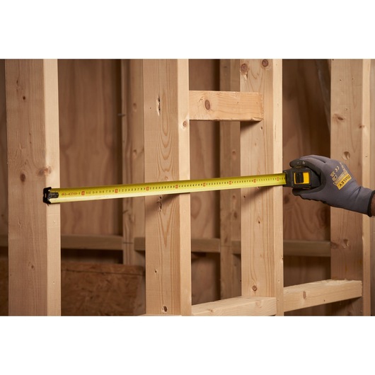 STANLEY STHT0-33566 tape measure in use measuring wooden studs at a construction site.