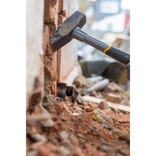 STANLEY STHT0-51910 hammer breaking brick wall, close-up on construction site.