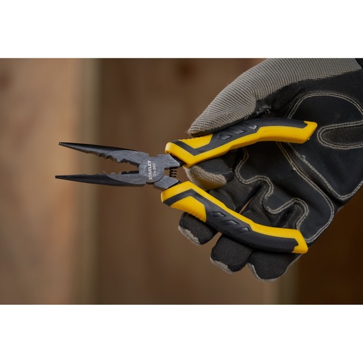 STANLEY STHT0-74364 pliers with yellow and black handles held in a gloved hand, close-up side angle.