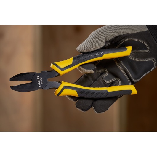STANLEY STHT0-74454 combination pliers with black and yellow handles held by gloved hand, close-up.