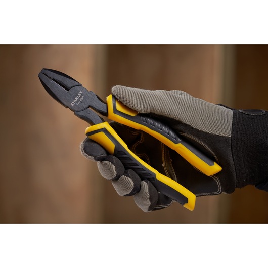Photo of STANLEY STHT0-74454 combination pliers with yellow and black handles, held in a gloved hand.
