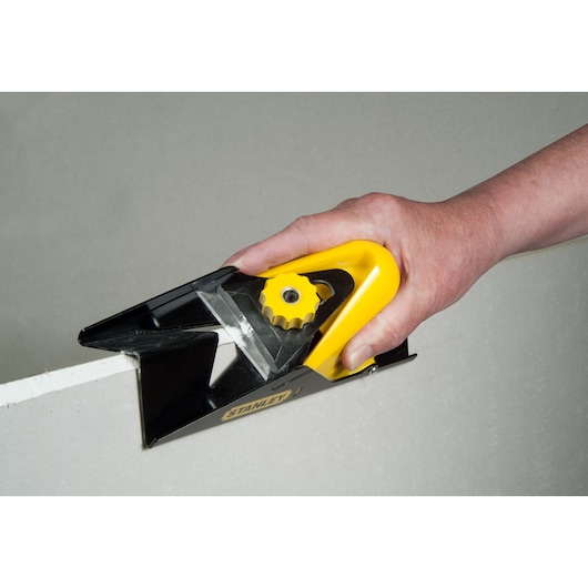 Photo of STANLEY STHT1-05937 hand-held plasterboard rasp in use on drywall edge.