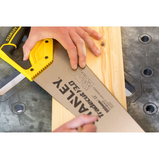 STANLEY STHT1-20353 handsaw with yellow handle cutting wooden plank on workbench.