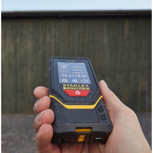 Photo of a STANLEY STHT1-77139 laser distance measurer held in hand, screen displaying measurement in meters.