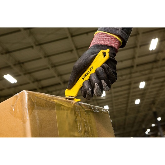 Stanley STHT10355-1 yellow safety utility knife used to cut box tape, close-up photography.