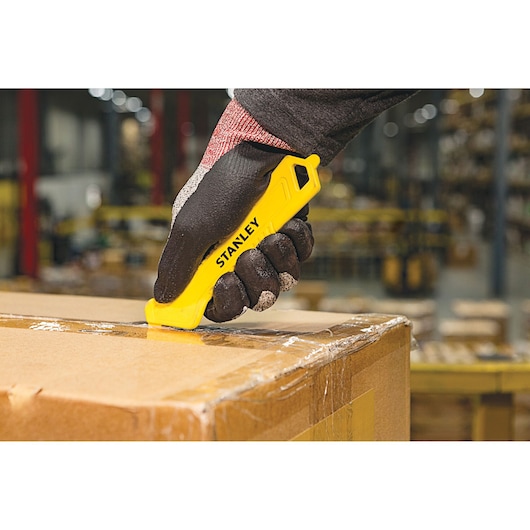 STANLEY STHT10355-1 safety utility knife cutting tape on a cardboard box in a warehouse, close-up.