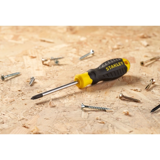 STANLEY STHT16155-0 Phillips screwdriver with black and yellow handle on wood with scattered screws.