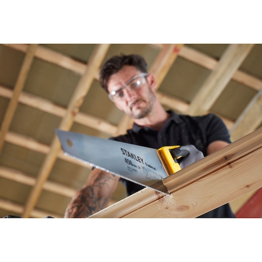 STANLEY STHT20355-1 hand saw with yellow handle cutting wood, angled close-up photography.