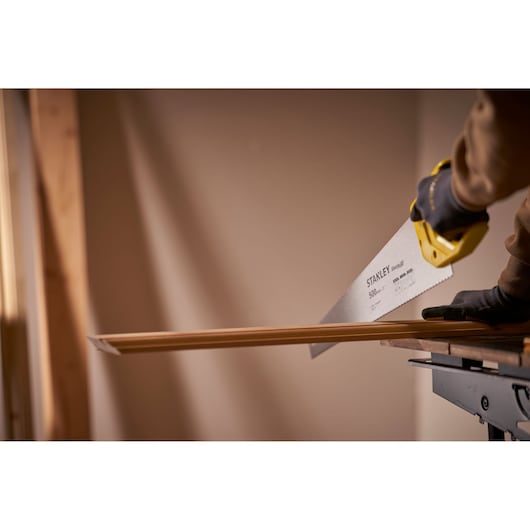 Photo of STANLEY STHT20371-1 hand saw cutting wood, yellow handle and gloved hand, indoor workspace.