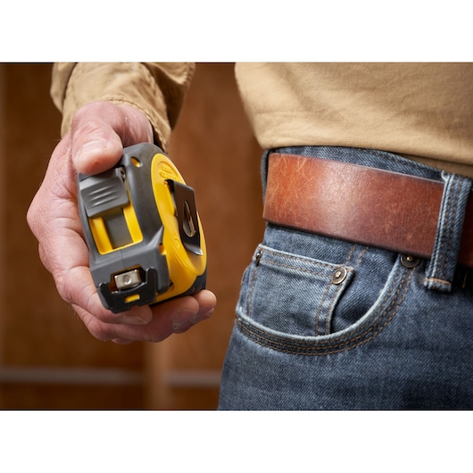 STANLEY STHT37233 tape measure with yellow and black casing held next to a denim pocket and brown leather belt.