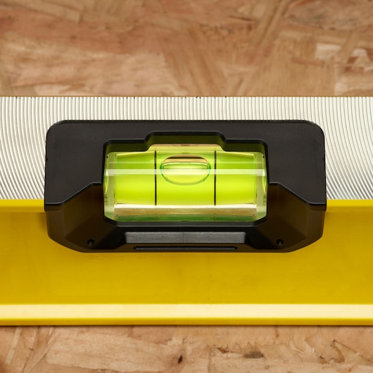 Close-up of a Stanley spirit level, showing the central bubble vial with yellow casing and black accents, placed on a wooden surface.