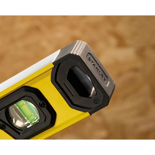 Close-up of a Stanley spirit level with a yellow body, black end cap, and visible bubble vial, used for measuring horizontal or vertical alignment in construction or photography.
