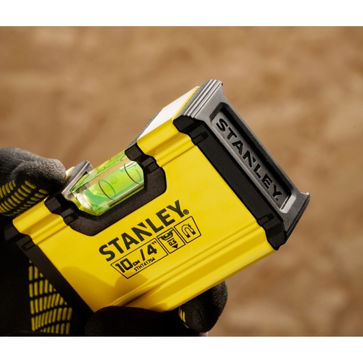 Close-up of a person holding a yellow STANLEY measuring tape with an integrated spirit level, showing product model STHT41704-0.