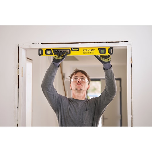 Person using a yellow STANLEY spirit level to check the alignment of a door frame indoors.