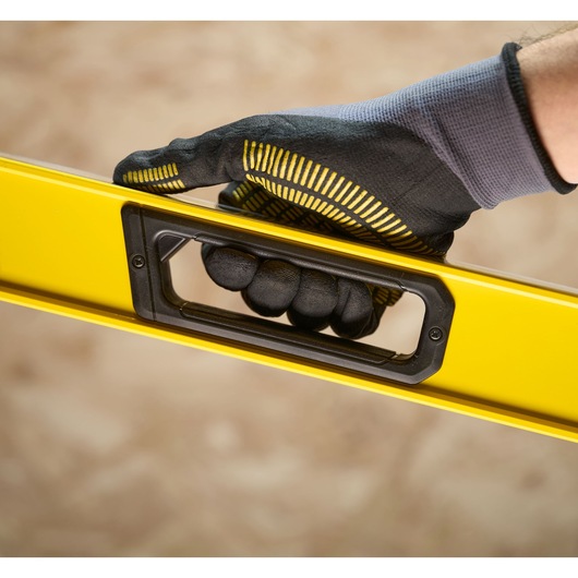 A gloved hand holding a yellow spirit level with a black handle.