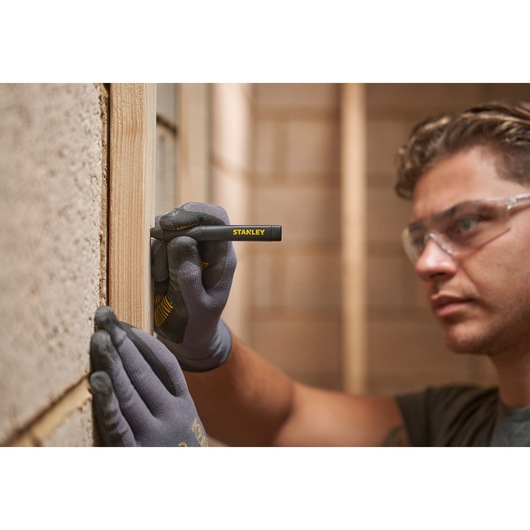 Person wearing gloves uses STANLEY marking pen to draw lines on wood during construction.