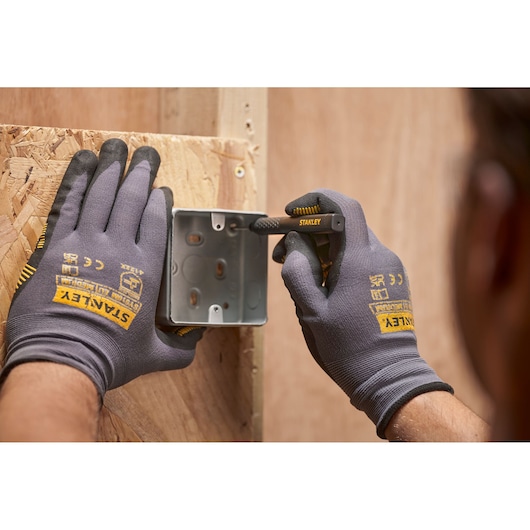 Hands with STANLEY gloves mark a metal box on wood using a STANLEY pencil during construction.