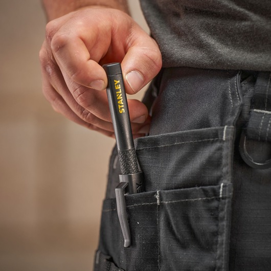 Hand placing a black Stanley marker into a front pocket on black work trousers.