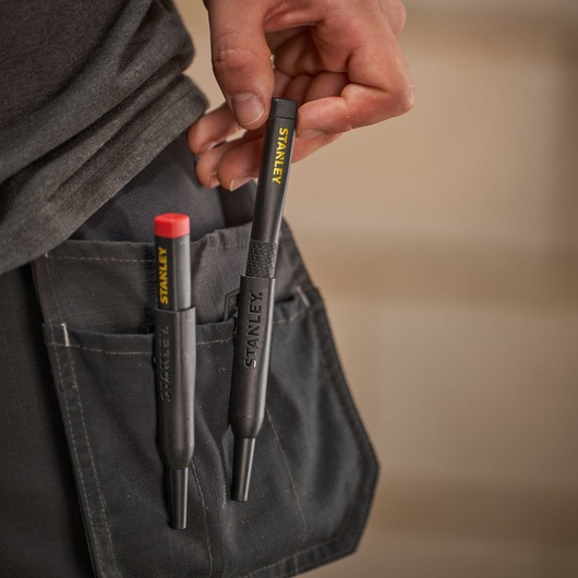 Two STANLEY marking tools in a work pocket, one being held by hand, designed for professional use.