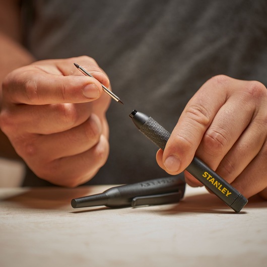 Hand holding a STANLEY pen with its refill being replaced, on a light surface.