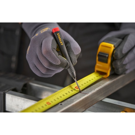 Gloved hands use a Stanley marking tool and tape measure to mark measurements on a metal surface.
