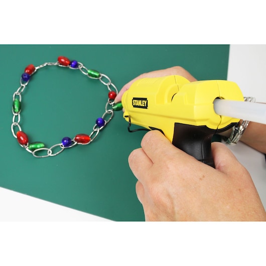 STANLEY STHT6-70417 yellow glue gun used to assemble a colorful beaded chain on a green surface.
