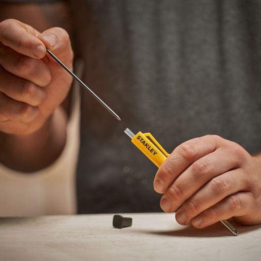 Hands holding a STANLEY yellow tool and metal shaft on a table. Tool is used for photography setup or repair.