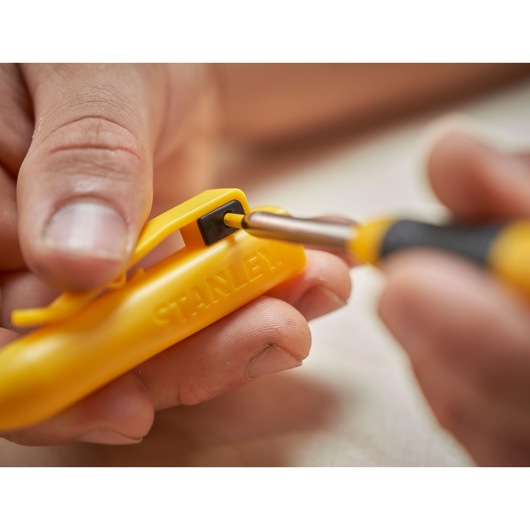 Close-up of hands using a yellow STANLEY tool with a black screwdriver tip inserted into its slot.