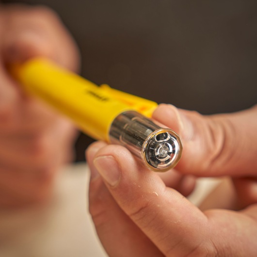 A close-up of a hand holding a yellow STANLEY voltage tester with a clear tip and metallic contacts.