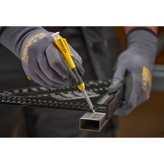 Gloved hands use a STANLEY marking tool and ruler to mark metal tubing for measurement or cutting.