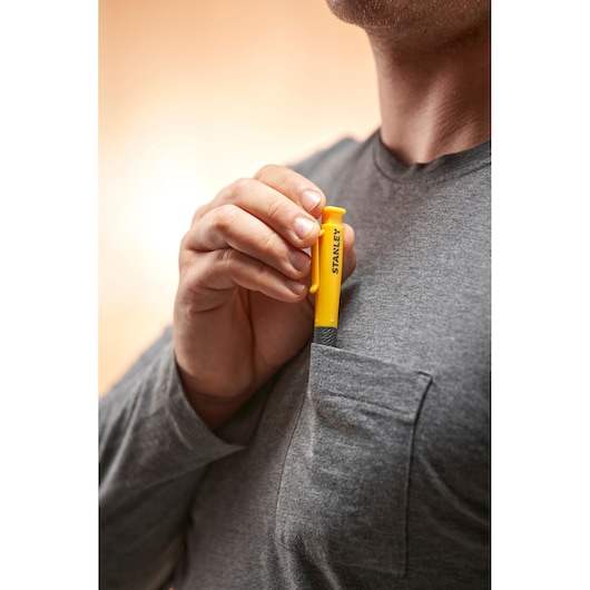 Person putting a yellow Stanley tool into the chest pocket of a grey shirt.