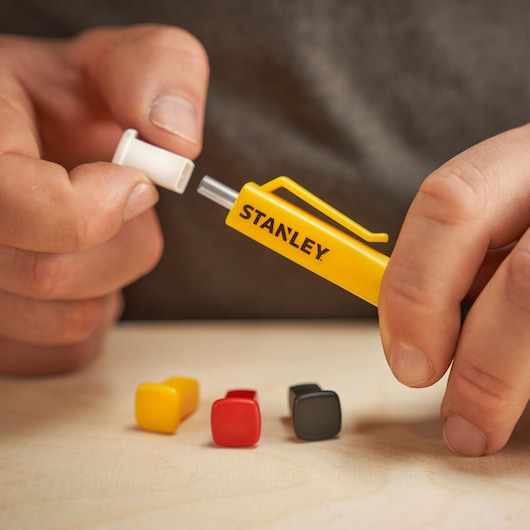 A hand holds a STANLEY yellow marking tool with color caps, used for photography marking on surfaces.